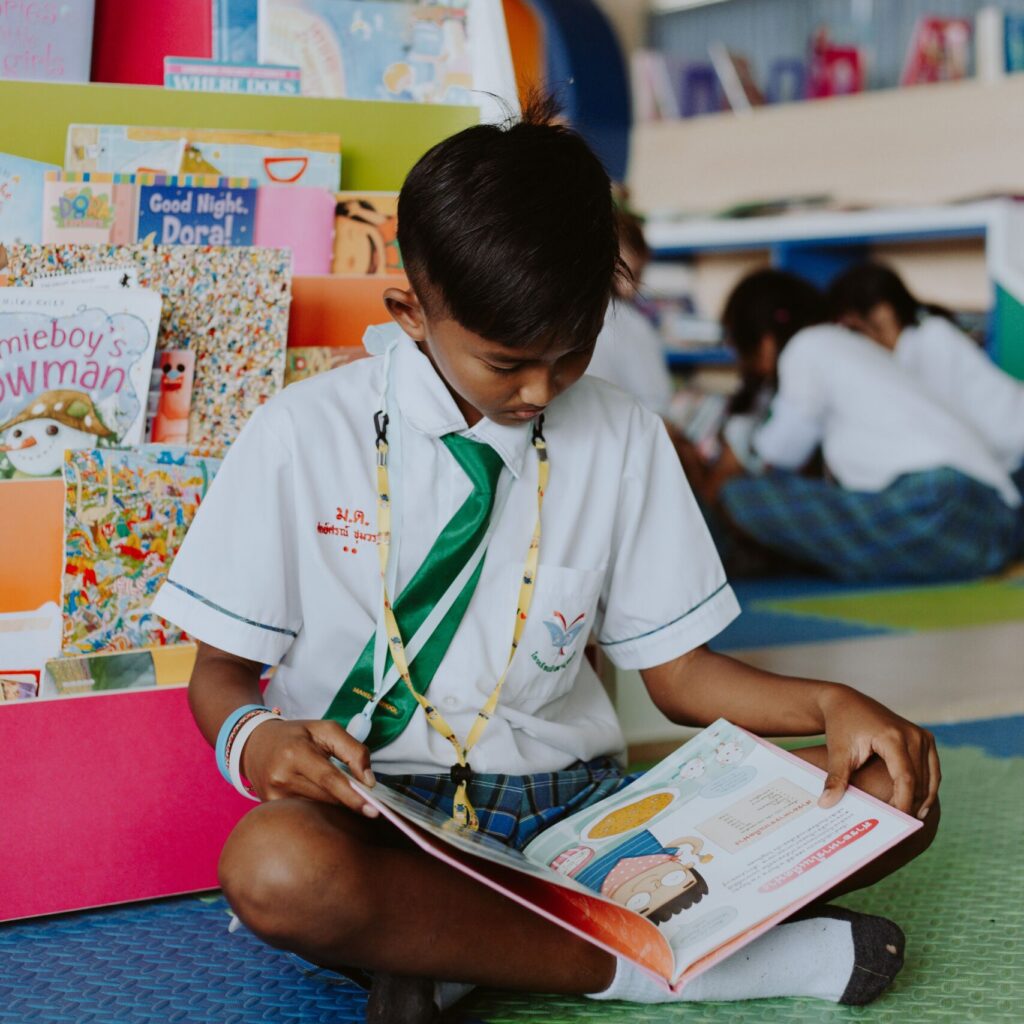 A young student reads intently on the library floor, surrounded by colorful children's books.
